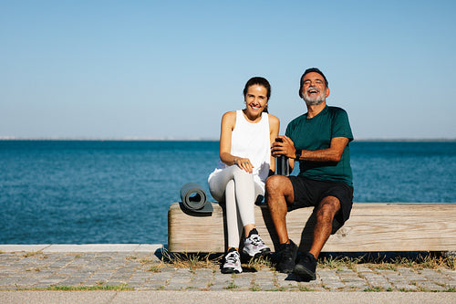 Smiling man and woman resting together on a scenic seaside wooden bench