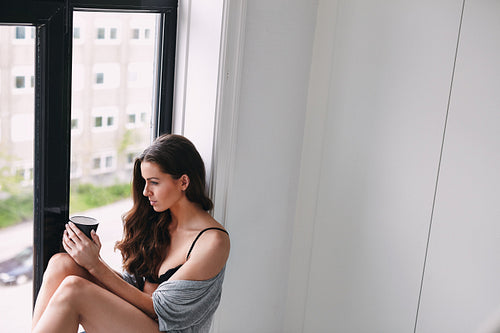 Female model in lingerie with her coffee mug by the window