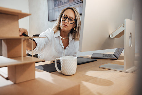 Architect examining a model at her office desk with a computer