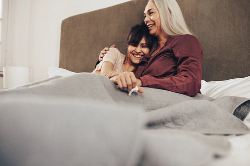 Smiling mother and daughter sitting on bed together covered in blanket