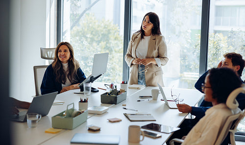 A woman stands presenting at a business meeting