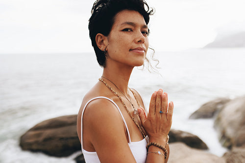 Woman in prayer pose looking serene at the beach during vacation