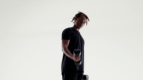 A focused man exercises with dumbbells building strength and muscle in a bright studio