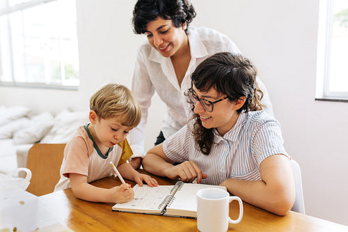 Female couple looking at their son scribbling in a book