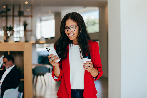 Businesswoman smiling while holding coffee and smartphone in an office environment