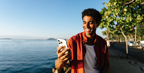 Young man using phone along Urca's Wall in sunny setting