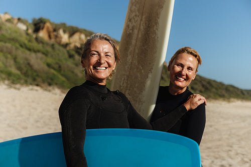 Two smiling friends holding their surfboards on the beach before surfing
