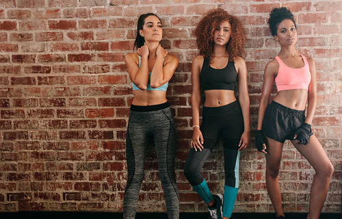 Three fitness women standing against brick wall 