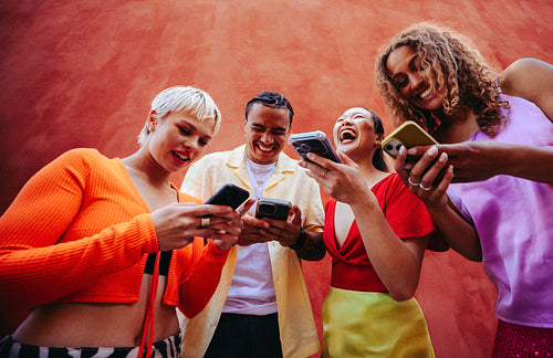 Sharing friends compare smartphone content together outdoors against a bright wall