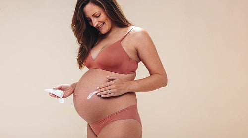 Happy pregnant woman applying antenatal belly cream for third trimester body care