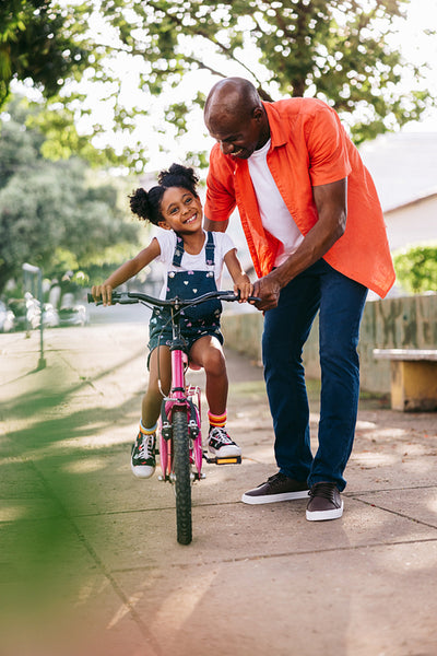 Happy father teaches daughter to ride a bike in sunny park
