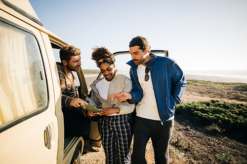 Friends on a coastal road trip viewing a map beside a vintage