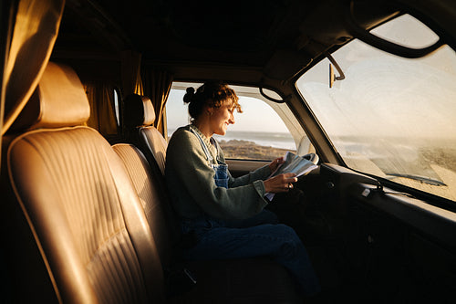 Woman driving and reading map inside a van by the coast