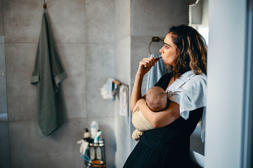 Mother brushes her teeth while holding baby