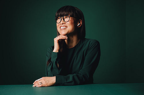 Confident mature Asian woman wearing glasses and earbuds in studio portrait