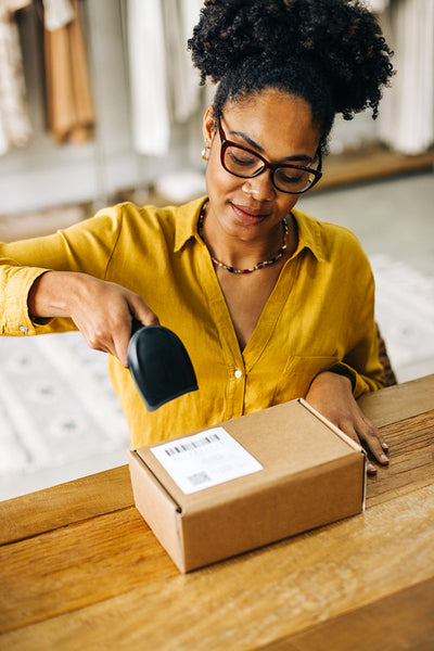Young black woman using a barcode scanner to process a package for dropshipping