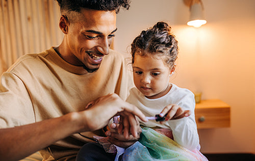 Adorable little girl applying nail polish on her dad's nails