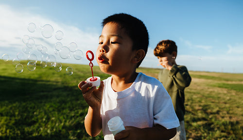 Young boy blowing bubbles in field with friend