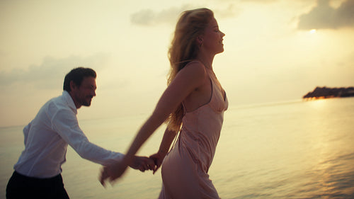 Romantic couple running playfully along beach at sunset