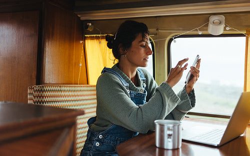 Woman using phone in a cozy camper with laptop nearby