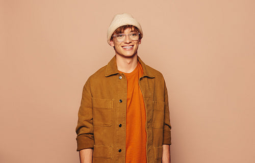 Smiling man in stylish urban denim jacket and glasses standing on vibrant peach background