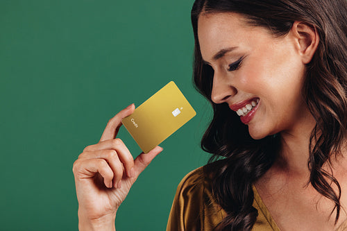 Enjoying cashless convenience. Woman smiles as she holds a gold credit card in a studio setting