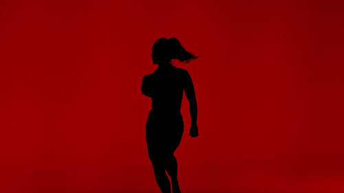Dynamic dance performance by a powerful woman silhouette against a vibrant red studio background