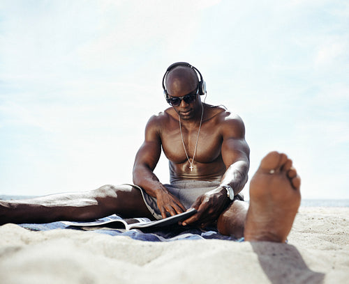 Young man sitting on beach reading a magazine
