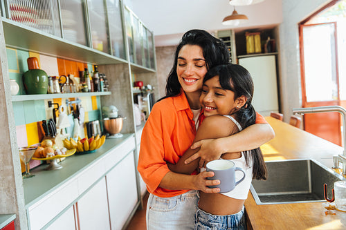 Latina mother and daughter hugging happily in their modern kitchen