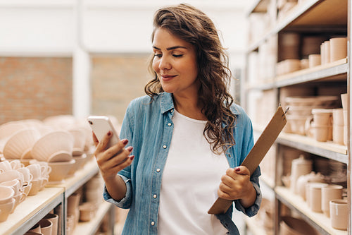 Creative businesswoman using a smartphone in her ceramic store