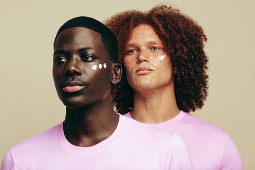 Two young men with unique skin tones use beauty cream on their faces
