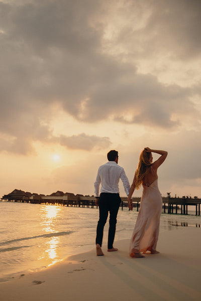 Romantic couple on honeymoon walking barefoot on sandy beach at sunset on tropical island