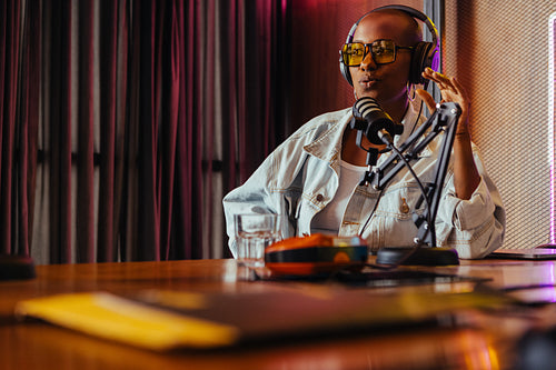 Confident female radio host recording in studio with neon light decor