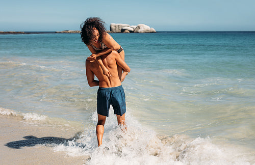 Man standing on beach carrying his girlfriend
