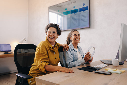 Two female colleagues laughing together in a friendly office setting