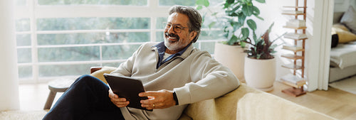 Senior man uses a tablet while seated on a sofa at home