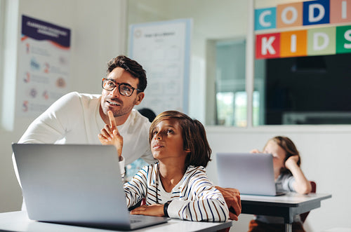 Teacher helping a young student with a coding exercise in a computer literacy class