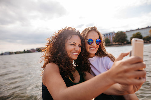 Female friends taking selfie with mobile phone by the lake