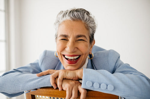 Success! Business woman smiling happily in her office, sitting on a chair and wearing a professional suit