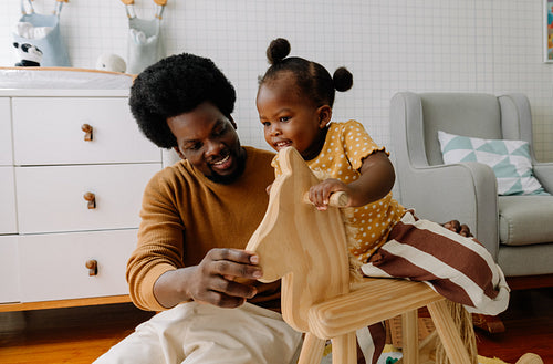 Dad and child play with wooden rocking horse