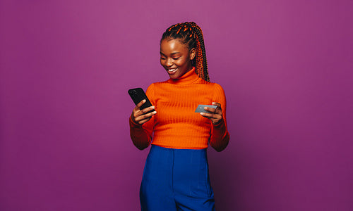 Happy gen z woman smiling and paying online with credit card on vibrant purple background