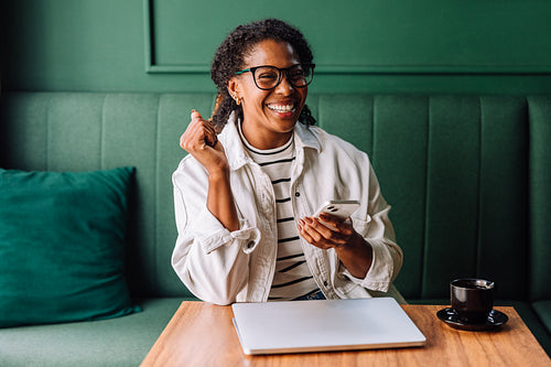 Happy black woman smiling while using smartphone in cafe