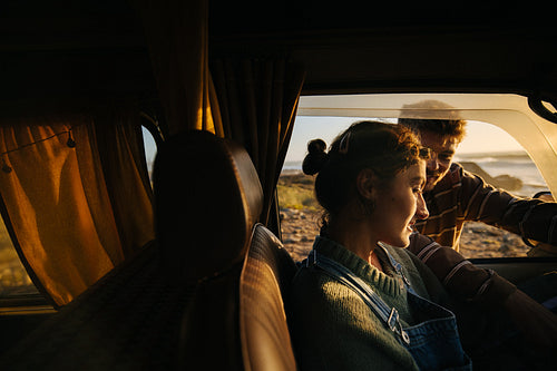 Couple in a camper van sharing a warm moment at sunset by the coast