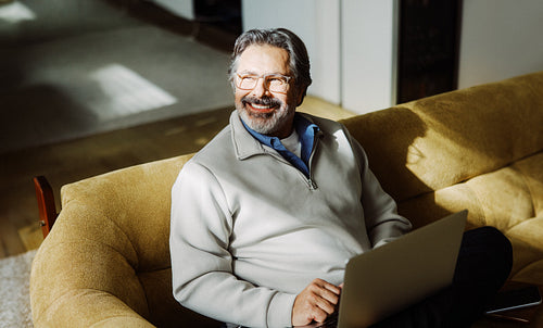 Senior man uses laptop while sitting on a sofa at home