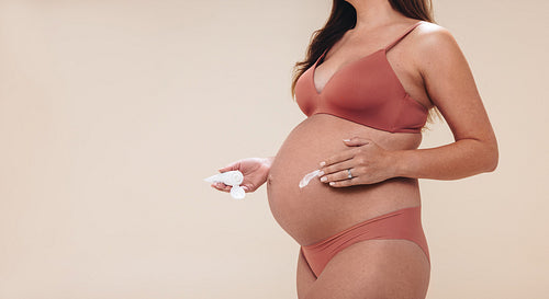 Pregnant woman applying skincare cream on her belly