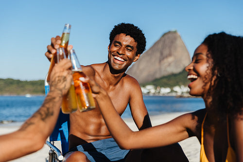 Joyful friends celebrating on a summer beach near Sugarloaf Mountain, sharing drinks and laughter under the bright sun