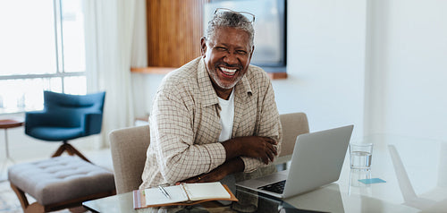 Modern Senior: Joyful businessman working from home using a laptop and notebook