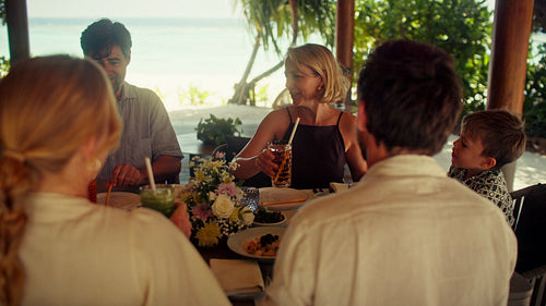 Happy family enjoying tropical breakfast with refreshing fruit juice at a beautiful resort villa