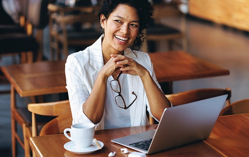 Happy professional woman working remotely in a cafe with laptop and coffee