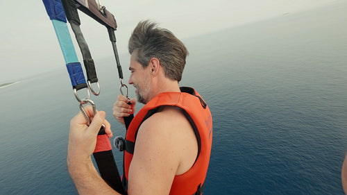 A man smiles while parasailing high above the vast blue ocean waters
